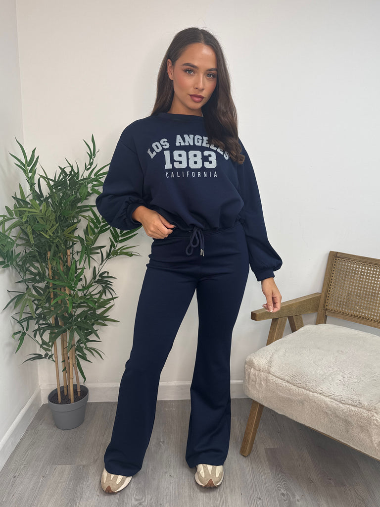 Model wearing Wholesale women’s navy Los Angeles 1983 sweatshirt and flared jogger co-ord set. Casual loungewear outfit for AW25 retail collections.